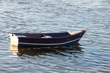 Kıyıdaki küçük mavi ve beyaz balıkçı teknesi ıslak kumda dinleniyor, enkazlarla çevrili.