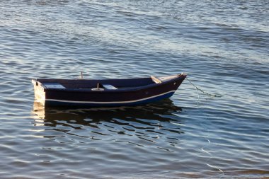 Kıyıdaki küçük mavi ve beyaz balıkçı teknesi ıslak kumda dinleniyor, enkazlarla çevrili.