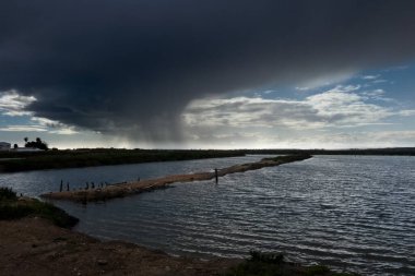 Tuz buharlaşması üzerine kara bulutlardan şiddetli yağmur yağması dramatik ve karamsar bir manzara yaratır.