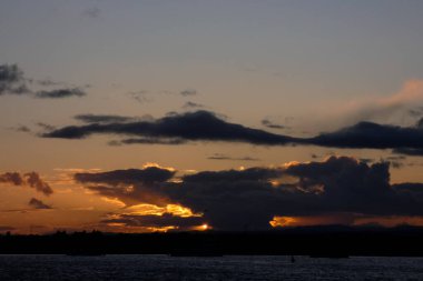 Parlak altın gün batımı, karanlık tepeleri aydınlatan bulutlar.