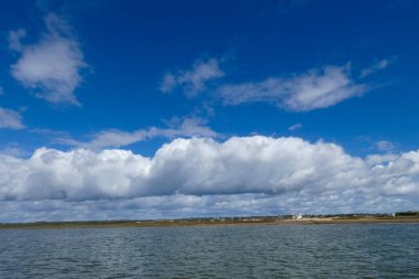 Güzel beyaz kümülüs bulutları, derin mavi bir gökyüzünde görülür. Huzurlu ve manzaralı bir manzara yaratır.