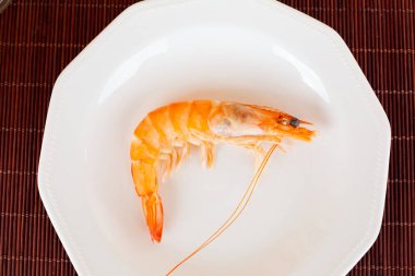 Tek pişmiş karides, beyaz bir tabakta servis altlığında, deniz ürünleri gibi tadını çıkarmaya hazır.