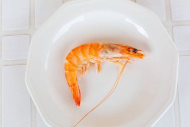 Tek pişmiş karides, beyaz bir tabakta servis altlığında, deniz ürünleri gibi tadını çıkarmaya hazır.