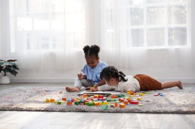 Evde oynayan iki kız çocuk. Yaratıcı olarak tahta blokla oynuyorlar. Afrikalı kız ve Asain kız birlikte eğleniyorlar..