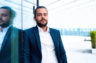 Takım elbiseli başarılı bir işadamı ofis binasının yanında dikilip kameranın zayıf duvarına bakıyor. İspanyol erkek iş adamı portresi. Boş alan. Modern İş İnsanları