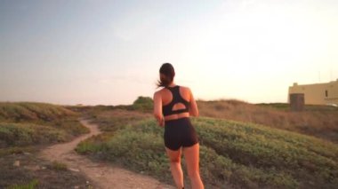 Doğada koşan bir kadın kırsal kesimde koşuyor. Sağlıklı koşu ve açık hava egzersizlerini, ağır çekim el kameralarını hesaba katın. Beyaz, orta yaşlı kadın koşucu gün batımında koşuyor.