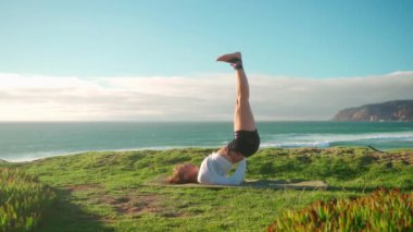 Arka planda okyanus manzaralı yoga egzersizleri. Kafkasyalı formda bir kadın deniz kıyısında yoga eğitimi alıyor. Sağlıklı yaşam tarzı kavramı. Yetişkin bir kadın yoga ve esneklik eğitimi alıyor.. 