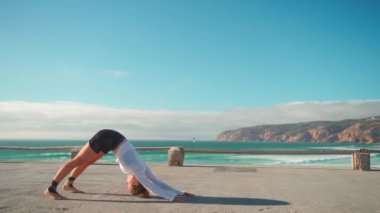 Arka planda okyanus manzaralı yoga egzersizleri. Kafkasyalı formda bir kadın deniz kıyısında yoga eğitimi alıyor. Sağlıklı yaşam tarzı kavramı. Yetişkin bir kadın yoga ve esneklik eğitimi alıyor.. 