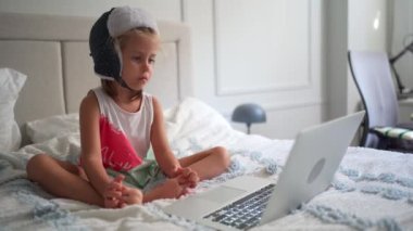 Komik şapkalı çocuk dizüstü bilgisayarda video izleyip evdeki koltukta oturuyor. Küçük beyaz kız laptopta yatak odasında oturan çizgi filmlerden hoşlanıyor. Neşeli anaokulu çocuğu dizüstü bilgisayar kullanıyor