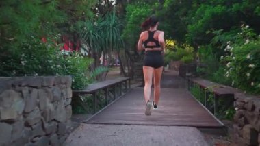 Orta yaşlı bir kadın, şehir parkının arka manzarasında yaz günü koşuyor. Beyaz kadın sporcu dışarıda koşuyor. Sağlıklı bir yaşam tarzı. Sabah koşucusu eğitimi. Dışarıda koşan zinde bir kadın. Tam uzunluk takip çekimi