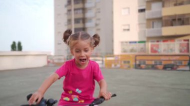 Güneşli bir yaz gününde şehirde bisiklet süren sevimli, gülümseyen bir kız. Çocuklarla aktif aile eğlencesi. Küçük beyaz kız 5 yaşında Pembe çocuk bisikletiyle eğlen
