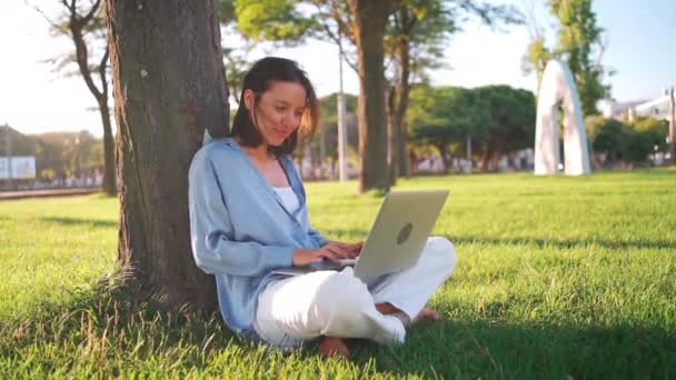 Щаслива Брюнетка Використовує Ноутбук Сидячи Біля Дерева Траві Парку Молода — стокове відео
