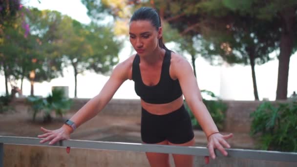 中年妇女在城市公园靠栅栏进行室外推拿运动 近视时穿着黑色运动服 欧洲女运动员在夏天进行锻炼 慢动作 — 图库视频影像