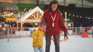 Anne ve kızı buz pateni pistinde el ele tutuşuyorlar. Annesi küçük kızına paten kaymayı öğretiyor. Kış Noel buz pateni pisti kış sporları, açık havada aktif boş günler.