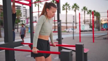 Paralel barlara triseps bandıran sportif formda bir kadın. Çekici beyaz kadın koşudan önce ısınıyor. Spor egzersizleri parktaki spor sahalarında açık hava. Güzel, sportif kadın..