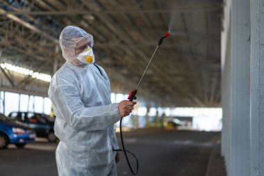 Koruyucu giysi giyen işçiler dezenfekte ekipmanları halka açık bir yerde park ediyorlar. Genel olarak dezenfektan güvenliği ve solunum maskesi Covid salgını önleyici tedbirler
