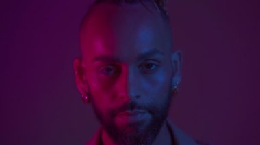 Neon light studio close-up portrait handsome black gay man looking camera. Seductive brazilian man wear make up, transgender person in ultraviolet light. LGBT nightclub and nightlife concept