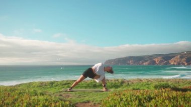 Arka planda okyanus manzaralı yoga egzersizleri. Kafkasyalı formda bir kadın deniz kıyısında yoga eğitimi alıyor. Sağlıklı yaşam tarzı kavramı. Yetişkin bir kadın yoga ve esneklik eğitimi alıyor.. 