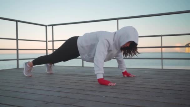 女运动员穿着连帽衫在户外运动 欧洲女运动员在海堤上锻炼 慢动作全长 健身动机 室外体育馆 — 图库视频影像