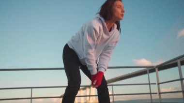 Woman boxer, wearing hoodie, rests after boxing outdoor training session. Confident and motivated, fit, healthy, and athletic female athlete practices boxing and kickboxing 