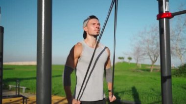 Erkek sporcu triseps kaslarını elastik bant ile çalıştırıyor. Atletik adam elastik direnç bandıyla triseps egzersizi yapıyor. Lastik bant sabit yatay çubuk. Spor, spor, spor yaşam tarzı.