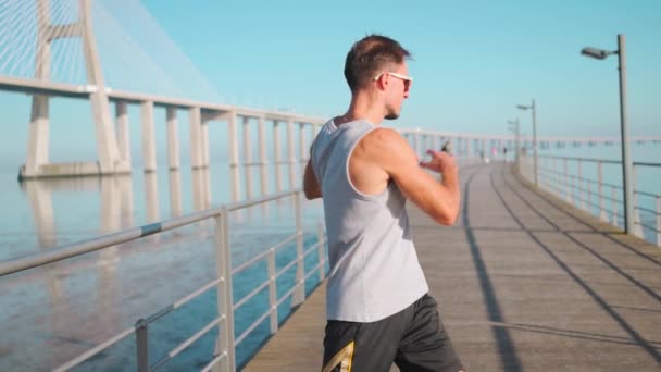 运动员在慢跑前热身 男子伸展双臂和胸部 然后站在夏天的蓝天背景上进行户外活动 — 图库视频影像