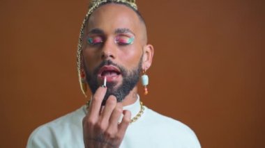 Homosexual man wear bright eyeshadow make up applies lipstick on lips. LGBT community with freedom for homosexuals. Black gay applying make up looking camera standing winking camera