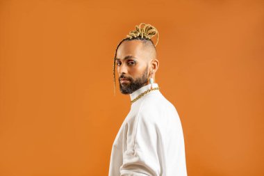 Confident black gay man with bright makeup standing isolated on orange background, dressed white. Exudes sense of pride and individuality. Diversity power of personal style. Side view