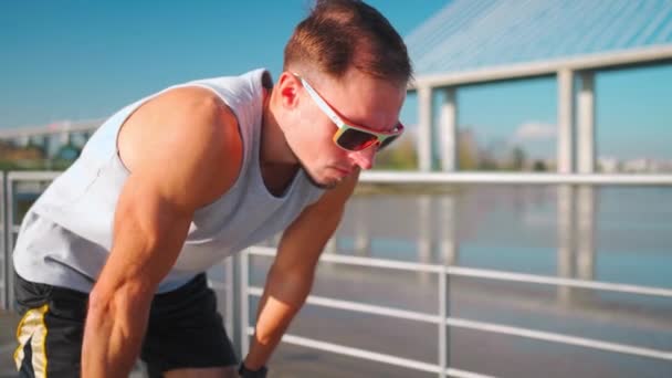 男子运动员在阳光明媚的天桥上跑步后 双手放在膝盖上 健美操训练后 运动员休息一下 呼吸练习早上的活动 健康的健身生活方式 — 图库视频影像