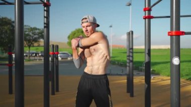 Atletizm sporcusu dışarıda vücut ısıtması yapıyor. Spor sahasında antrenmandan önce kollarını ve göğsünü geren formasız bir adam. Modern jimnastik parkında uygun erkek esneme egzersizi.