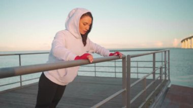 Athlete female doing push up exercises outdoor leaning on fence dressed hoodie sportswear. European athletic female practicing workout day. Slow motion close up. Fitness motivation, gym outdoor