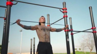 Erkek sporcu triseps kaslarını elastik bant ile çalıştırıyor. Gömleksiz atletik adam elastik direnç bandıyla göğüs egzersizi yapıyor. Lastik bant sabit yatay çubuk. Spor, spor, spor.