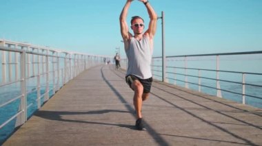 Athletic person warming up body before jogging exercise. Man stretching legs doing lunges before running training outdoors standing on bridge summer day blue sky background