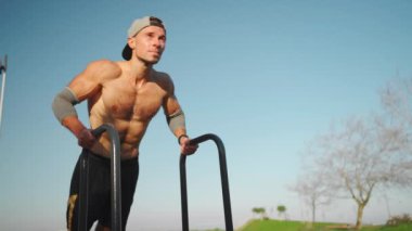 Muscular man doing push ups exercises on parallel bars. Male athlete workout outdoor gym, Strength and motivation. Medium shoot front view. Bodyweight training. Modern calisthenics park