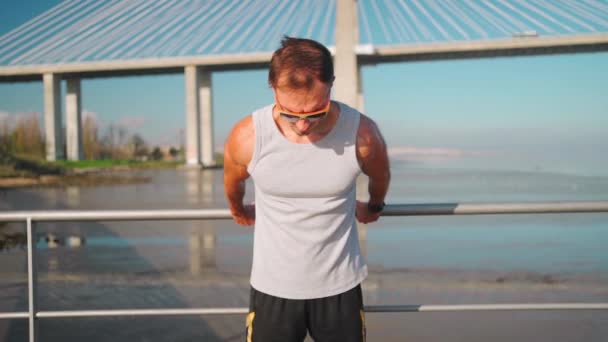 运动员在慢跑前热身 男子伸展双臂和胸部 然后站在夏天的桥上进行室外训练 — 图库视频影像