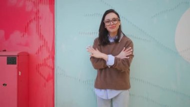 Gözlüklü mutlu kadın parmaklarını şaklatıyor. Renkli duvarların yanında duruyor. Gülümsüyor ve bir şeyler söylüyor. Pozitif kadın saçını düzeltir Bir hikaye anlatır 