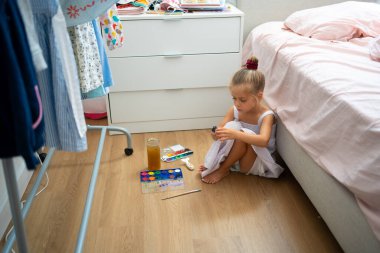 Caucasian child girl is painting watercolor paint on small ceramic figure with fun. Kids arts and crafts creative activity class at home. Little girl make ceramic decor sitting floor