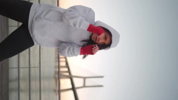 橋と青空の背景を持つ赤いボクシングテープに包まれた女性ボクシングの手 中世の女性アスリートの戦闘機の訓練はパーカーを着て外 垂直ビデオ — ストック動画
