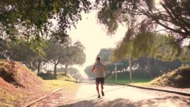 Erkek koşucu, güneşli bir parkta koşuyor. Şehir parkında kardiyo antrenmanı yapan bir sporcu. Sabah sağlık aktivitelerinde gerçek insanları eğitmek.