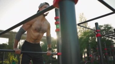 Şınav çeken kaslı adam yatay çubuklar kullanıyor. Açık havada spor yapan üstsüz bir sporcu, güç ve motivasyon. Orta ölçekli atış. Vücut ağırlığı eğitimi. Modern beden eğitimi parkı