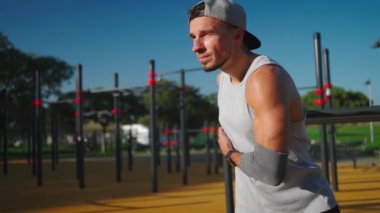 Modern jimnastik parkında vücudunu esneten atletik bir adam güneşli bir yaz günü. Formda bir insan vücut egzersizi yapıyor. Sabah antrenmanı rutini. 
