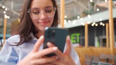 Akıllı telefonlar kullanan bir kadın. Gözlüklü bir kadın alışveriş merkezinin yanında cep telefonu kullanıyor. Akıllı telefon görünümlü cihaz ekranlı internet tarayıcısı olan mutlu kadın serbest yazar