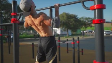 Atletik adam yatay barın önünde durur. Tişörtsüz erkek atlet parktaki spor sahasında takılıyor. Fitness, spor, güç egzersizi, eğitim ve yaşam tarzı kavramı
