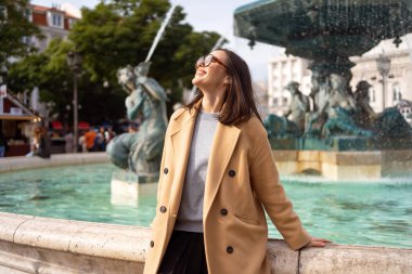 Portekiz 'in başkenti Lizbon' da eğlenen kadın turist. Güneşli bir gün. Avrupa seyahati konsepti. Praca Dom Pedro IV veya Rossio Meydanı, Lizbon 'daki barok fıskiyelerin önünde oturan şık giyinmiş bir kadın..