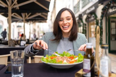 Kafe masasında salata yiyen gözlüklü bir iş kadını. Güzel orta yaşlı kadın güzel bir restoranın terasında taze salata yiyor..