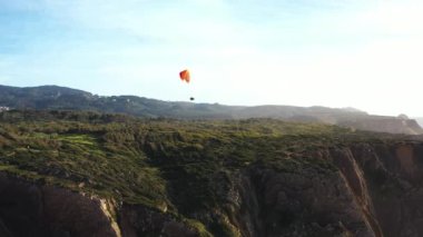 Uçsuz bucaksız mavi gökyüzünde, sinematik deniz mavisi okyanusuna doğru uçan olağanüstü bir paraglider. Tanınmayan kişi Atlantik Okyanusu yakınlarında paraşütle uçuyor.