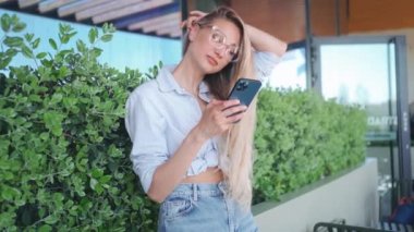 Sokak Fotoğrafı: Akıllı Telefon Kullanan Güzel Kadın Portresi. Gülümseyen, uzun sarı saçlı, gözlüklü, internetten alışveriş için cep telefonu kullanan, e-ticaret yapan bir girişimci.. 