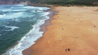 Portekiz Praia da Guincho 'da Atlantik Okyanusu sahilinde fırtınalı güneşli bir yaz günü. Güzel deniz manzarası. Kumlu sahilde hava manzarası 