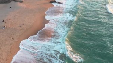 Sonbahar günü okyanus sahilinde hava manzarası, üstgeçit kumlu beac ve turkuaz su, güneşli bir günde yürüyen insanlar. Portekiz 'deki Guincho plajı.