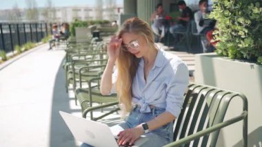 Bilgisayarla uzaktan çalışan kız öğrenci, terasta oturan kafe koltuğu. Kadın kafe masasında oturuyor, dizüstü bilgisayar kullanıyor ve ekrana bakıyor. Uzak işleri, boş yerleri ara